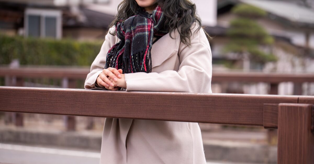 冬の街でマフラーを巻いた女性が橋の手すりにもたれる様子