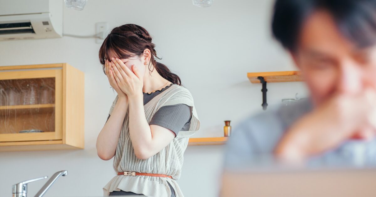 キッチンで顔を覆い落ち込む女性と後ろで悩む男性のすれ違い