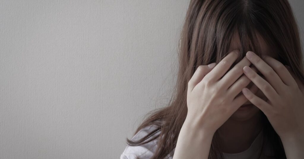 手で顔を覆い涙をこらえる女性のストレスや悲しみのイメージ