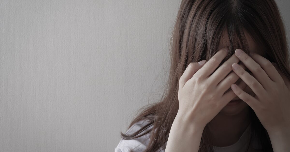 手で顔を覆い涙をこらえる女性のストレスや悲しみのイメージ
