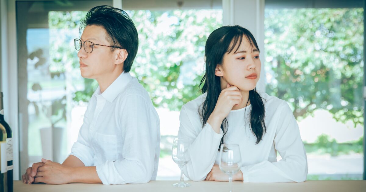 テーブルで背中合わせに座る男女の冷え切った関係イメージ