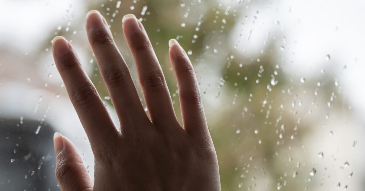 雨の窓に手を当てる女性の孤独や悲しみのイメージ