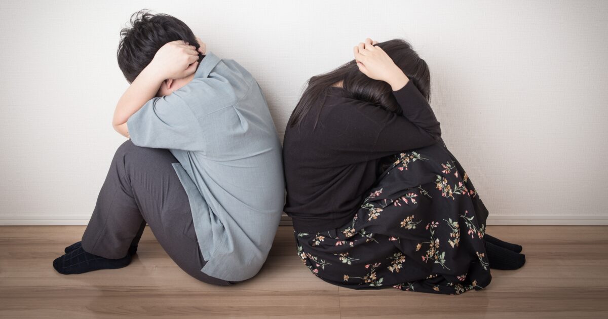 床に座り頭を抱える男女の深刻なトラブルや不安のイメージ