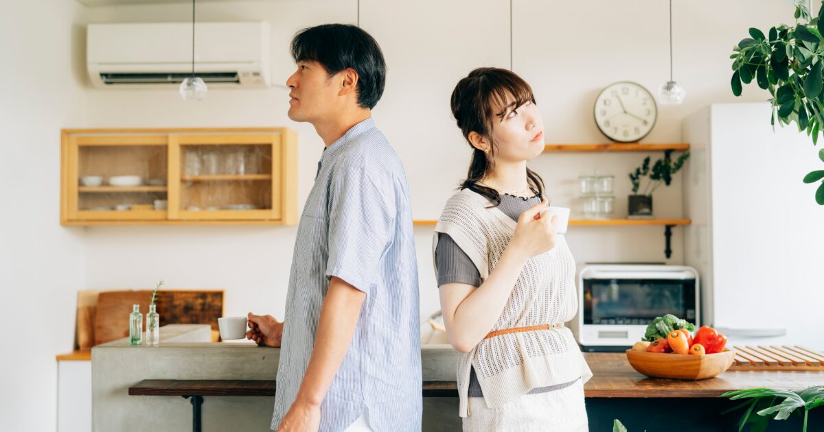 キッチンで背中合わせに立つ夫婦の不仲イメージ