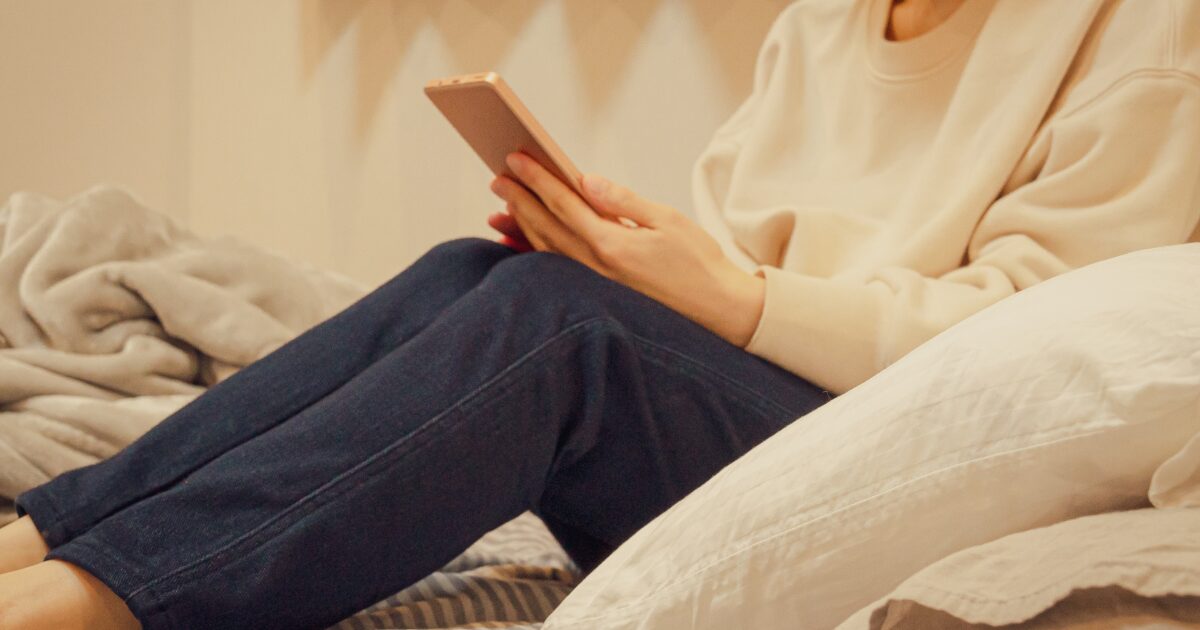 ベッドでスマートフォンを見るリラックスした女性の手元