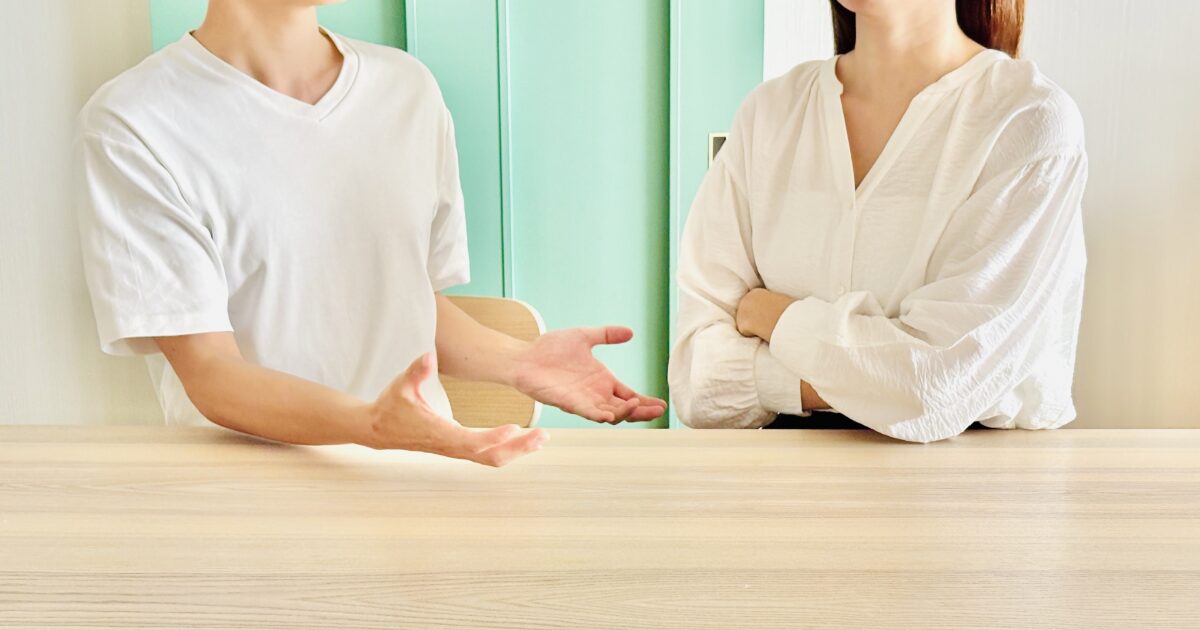 テーブル越しに話し合うカップルのすれ違いイメージ