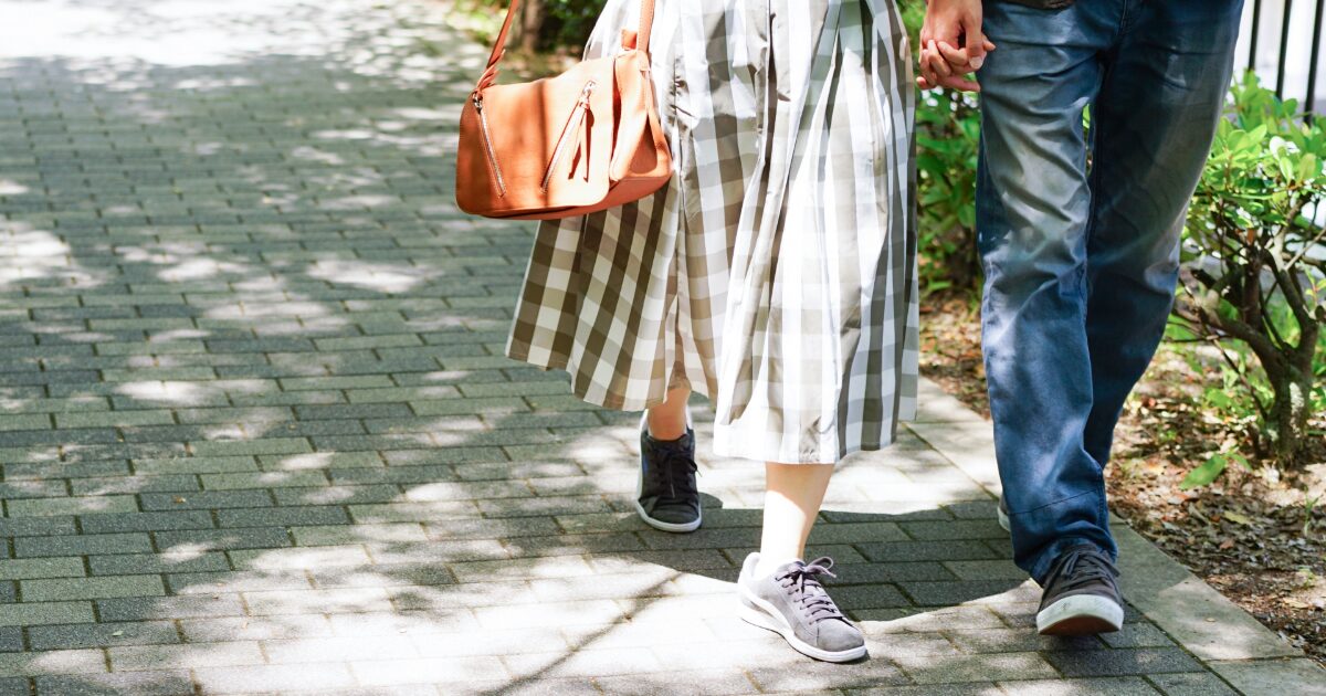 公園の遊歩道で手をつないで歩くカップルの足元